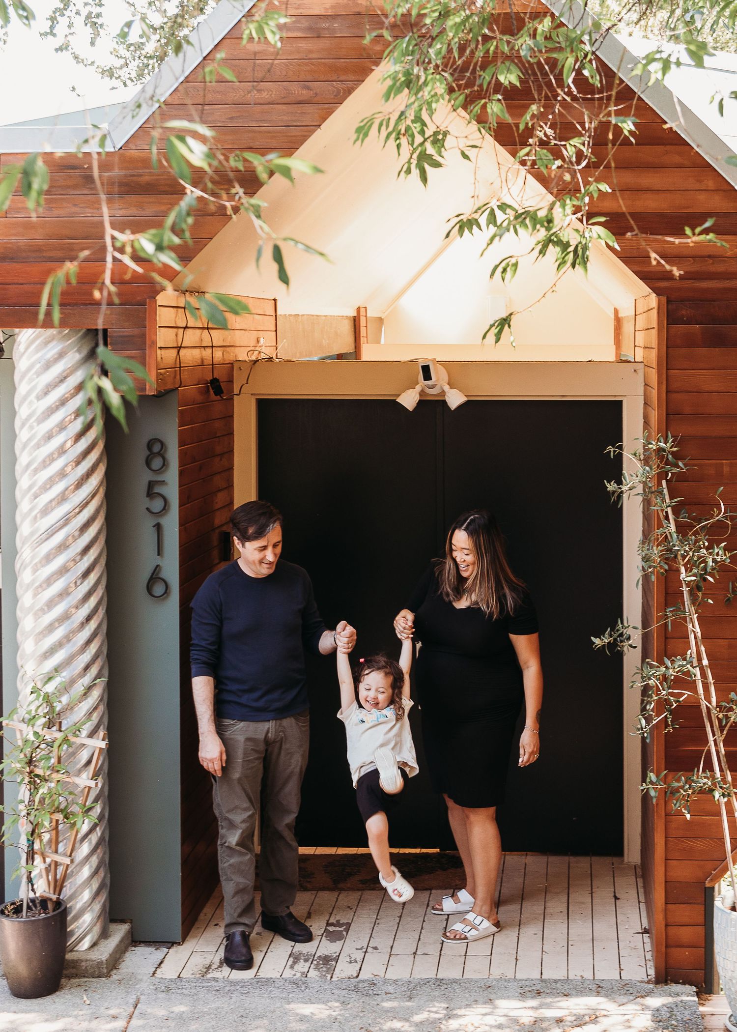 A playful family moment on a wooden porch with hanging plants.