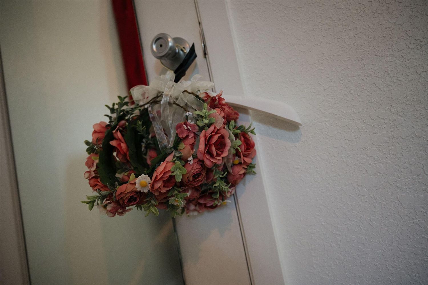 A decorative floral wreath with pink roses hanging on a white wall.