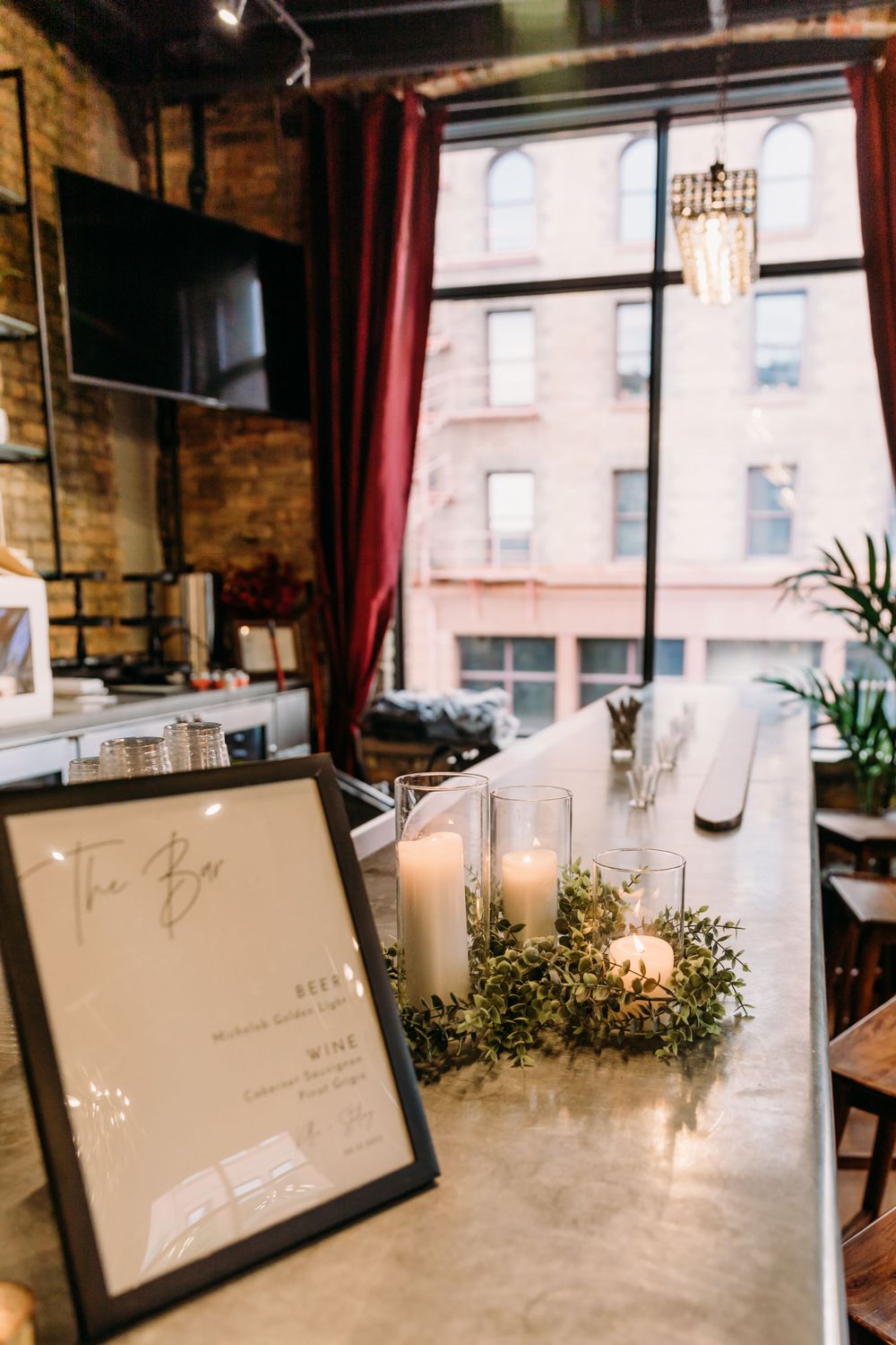Wedding reception table settings with framed signs and candlelight against exposed brick walls.