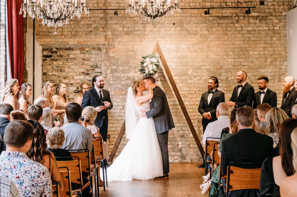 Wedding ceremony in a rustic brick venue with elegant chandeliers overhead.