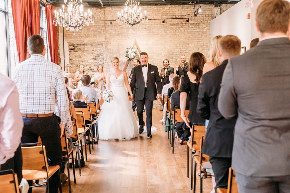 Wedding guests seated in rows at ceremony venue with exposed brick walls and chandeliers.