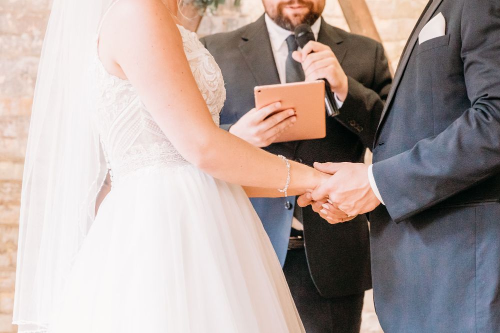 Close-up of hands exchanging rings during wedding ceremony with wooden arch in background.