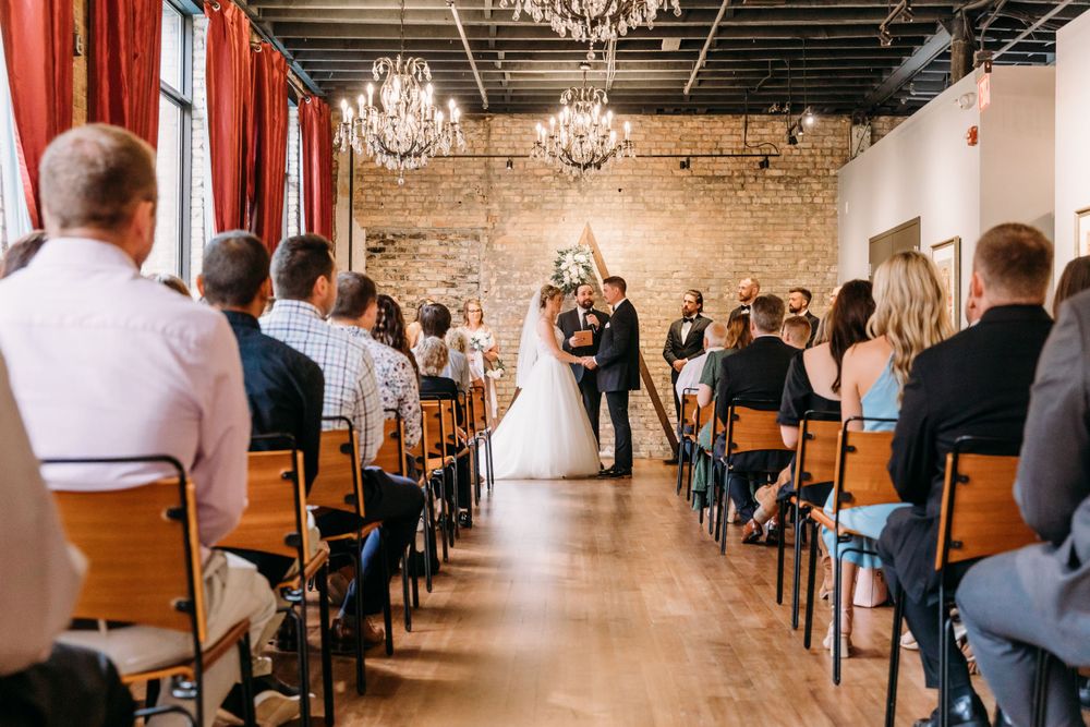 Wedding ceremony in progress in a rustic venue with exposed brick walls and chandeliers.