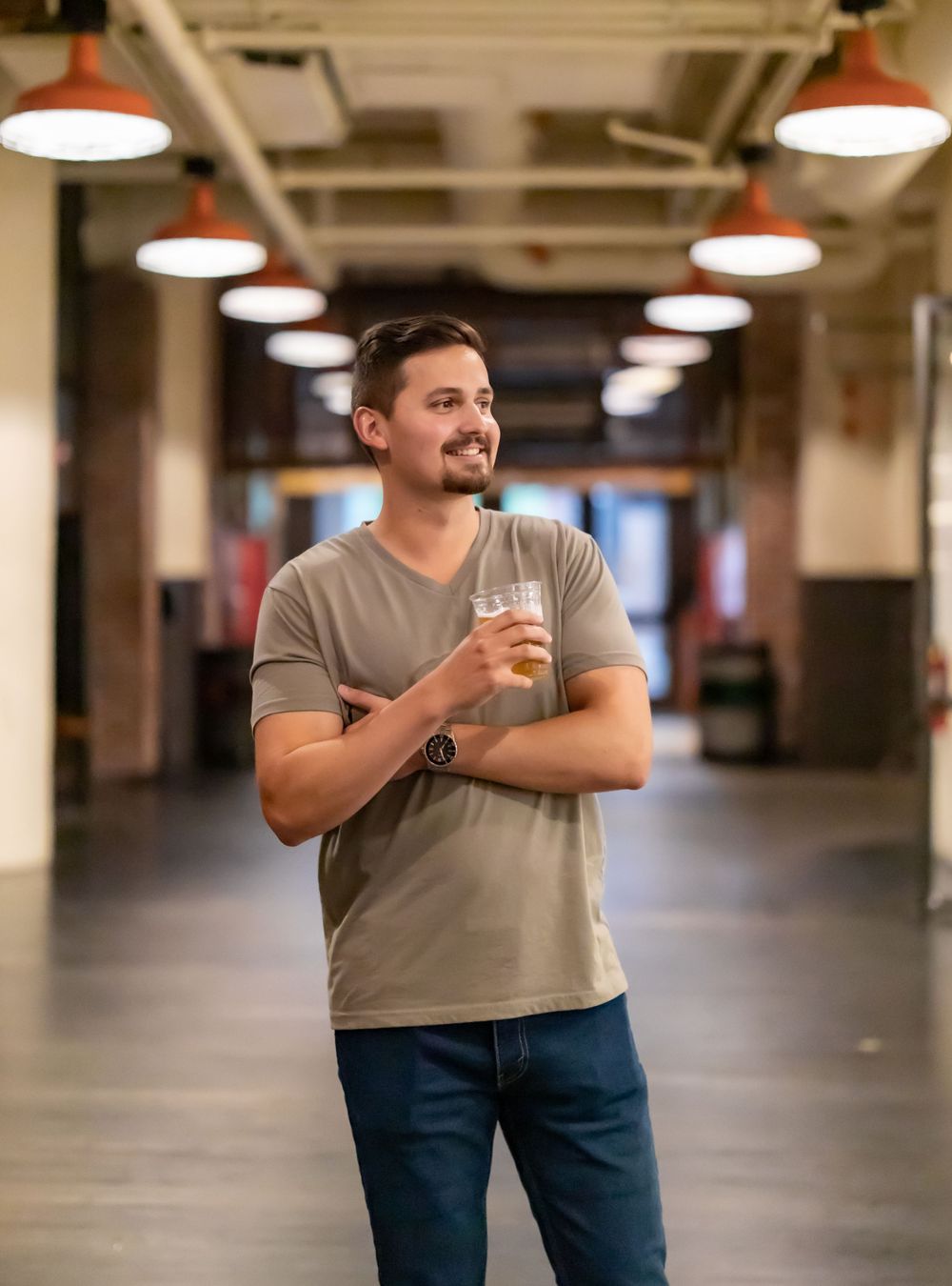 Person in gray shirt poses in industrial space with overhead lighting.