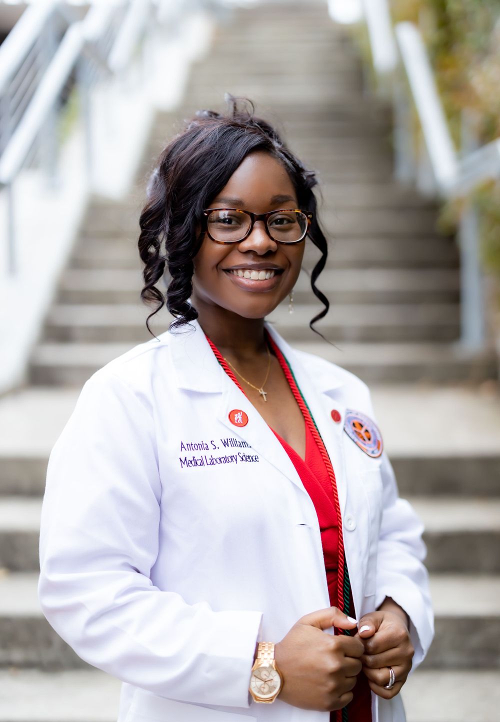 A professional in a white lab coat and glasses poses confidently on outdoor stairs.