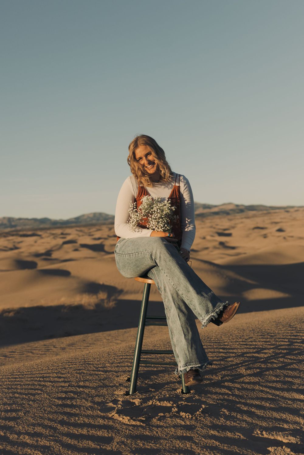 A person sitting on a stool in desert sand dunes during golden hour.