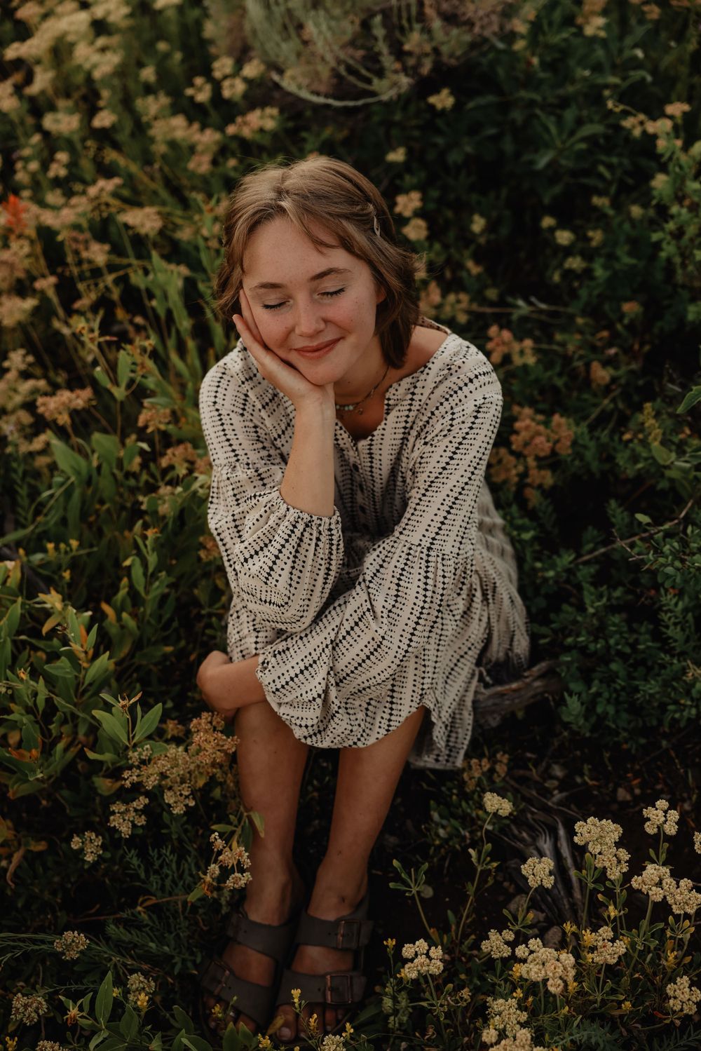 Cozy portrait of someone in a chunky knit sweater sitting among wildflowers at sunset.