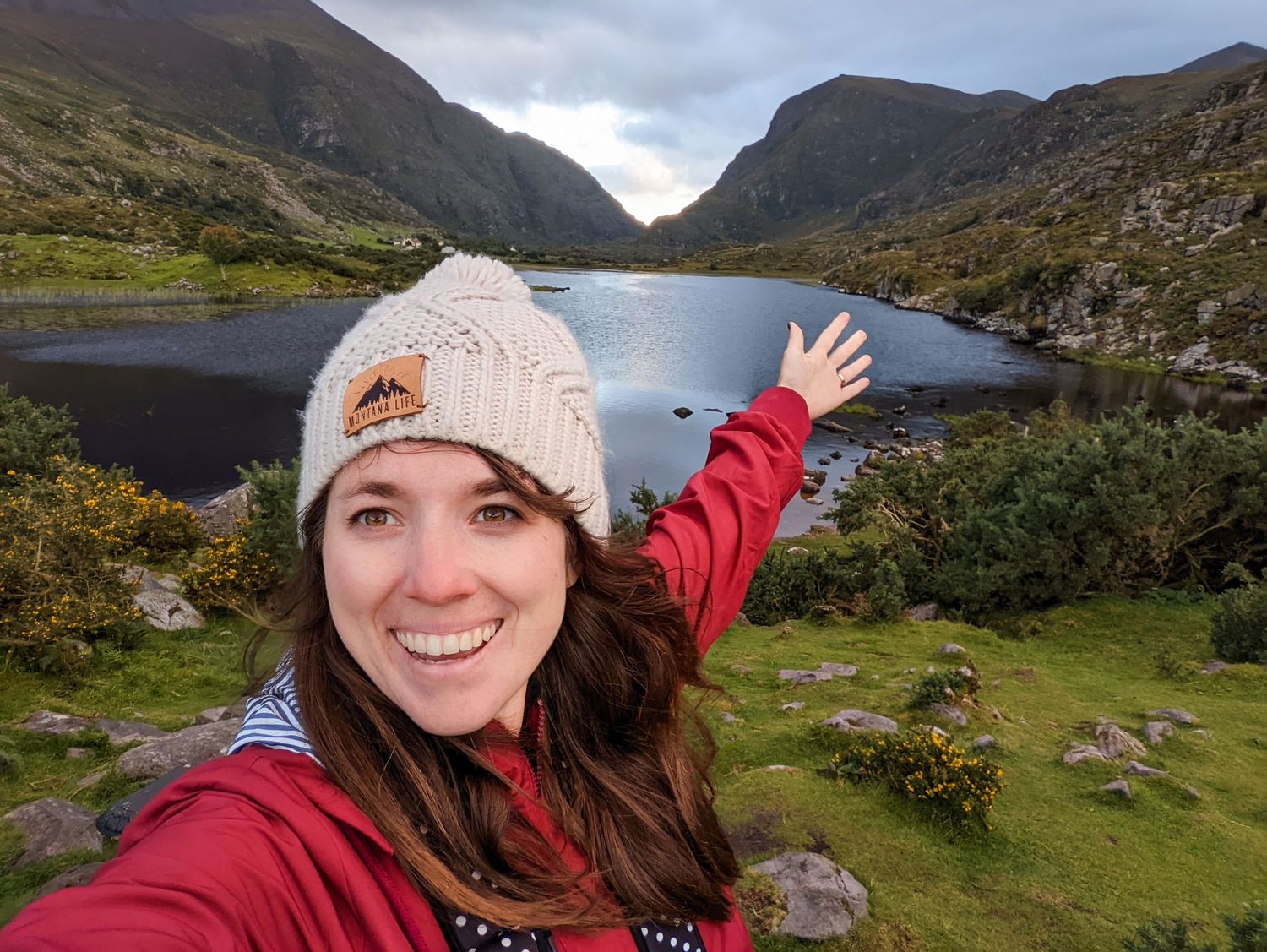 A hiker waves at scenic mountain lake view in Ireland with green hills.