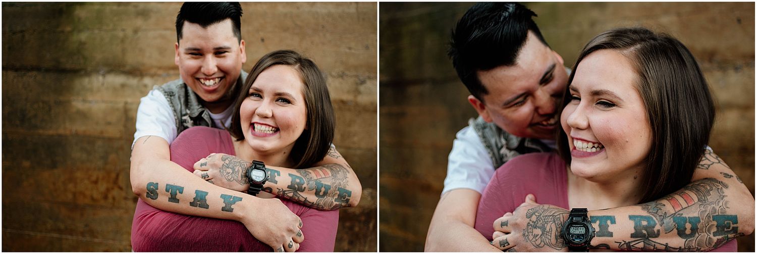 Happy couple laughing together while embracing against textured brown wall.