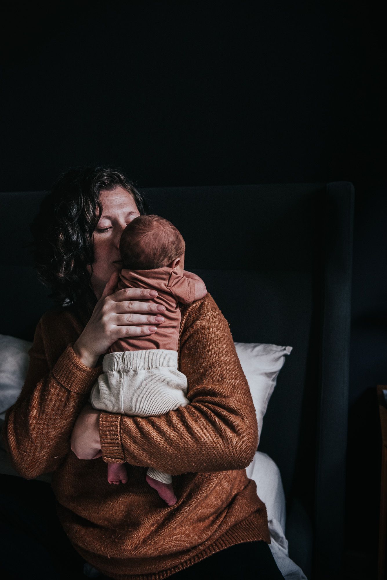 Wee little newborn being held by his mama, who is kissing his little head.