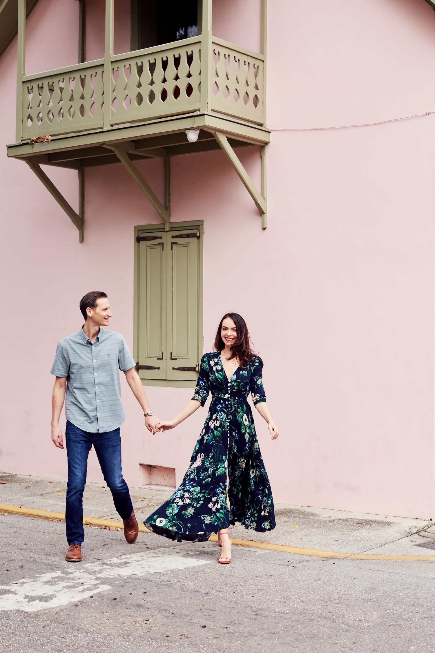 Couple walking hand in hand by pink building with ornate balcony in historic district.