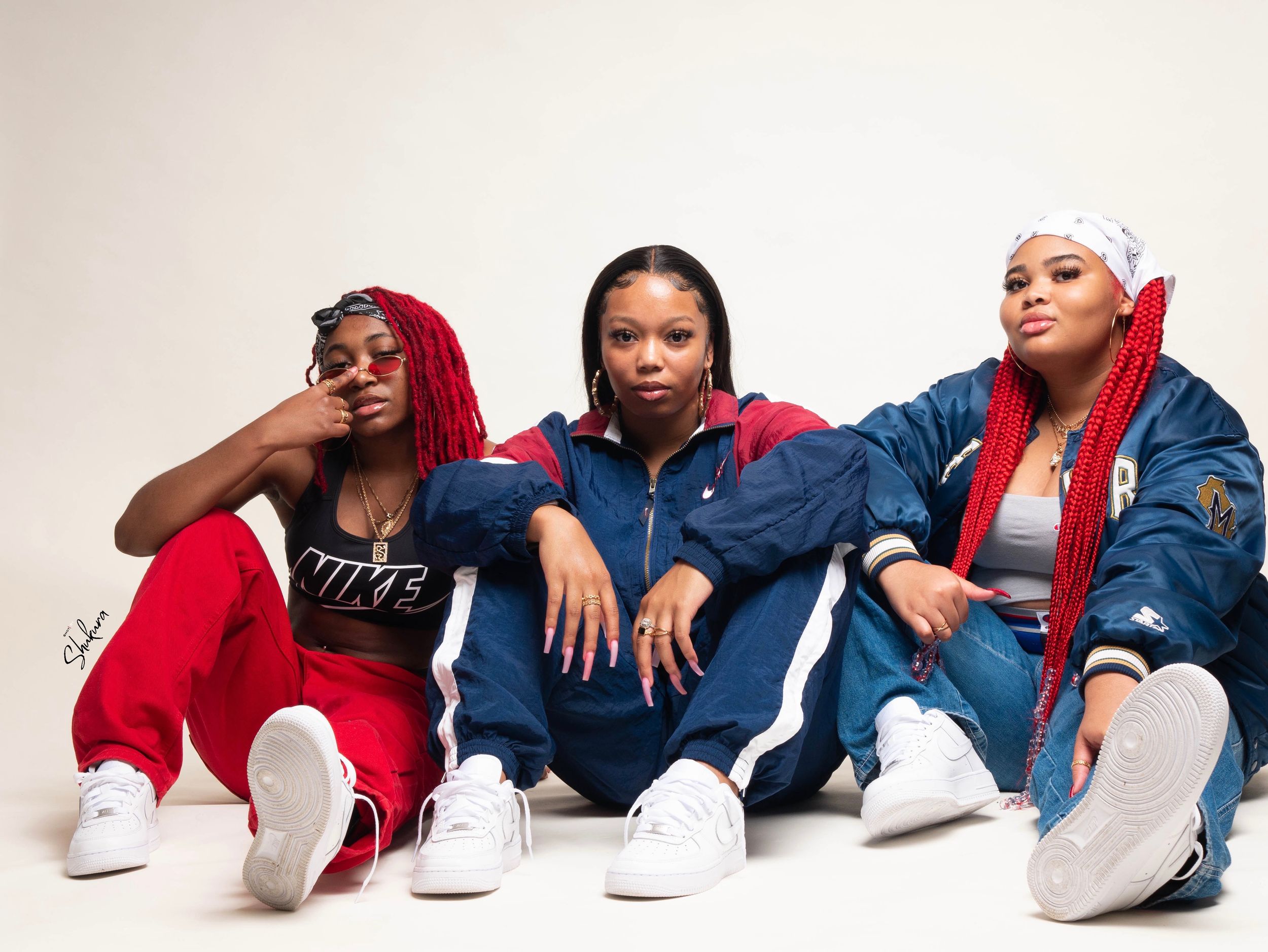 Three people in casual streetwear pose together against white background.
