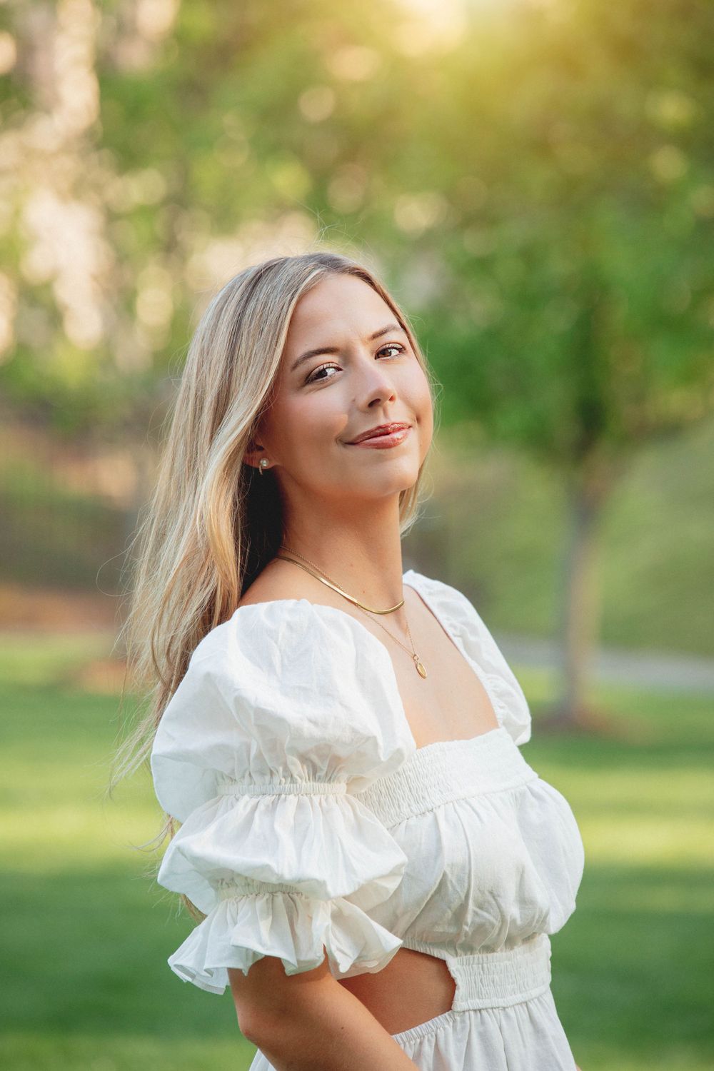 Portrait of woman in white dress with puffy sleeves posing in outdoor garden setting.