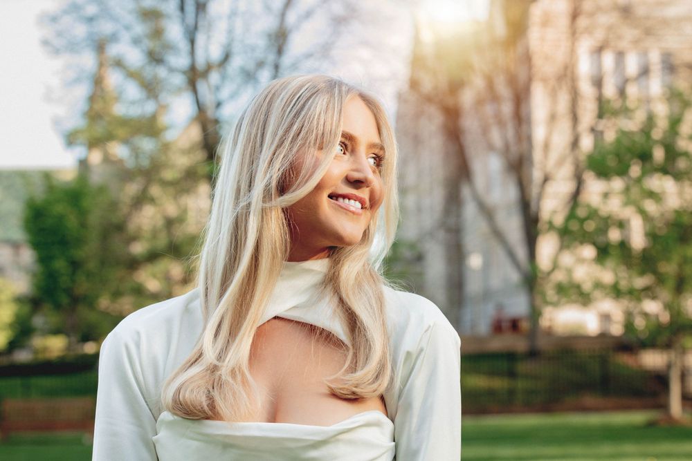 Outdoor portrait with natural sunlight highlighting woman in cream colored top.