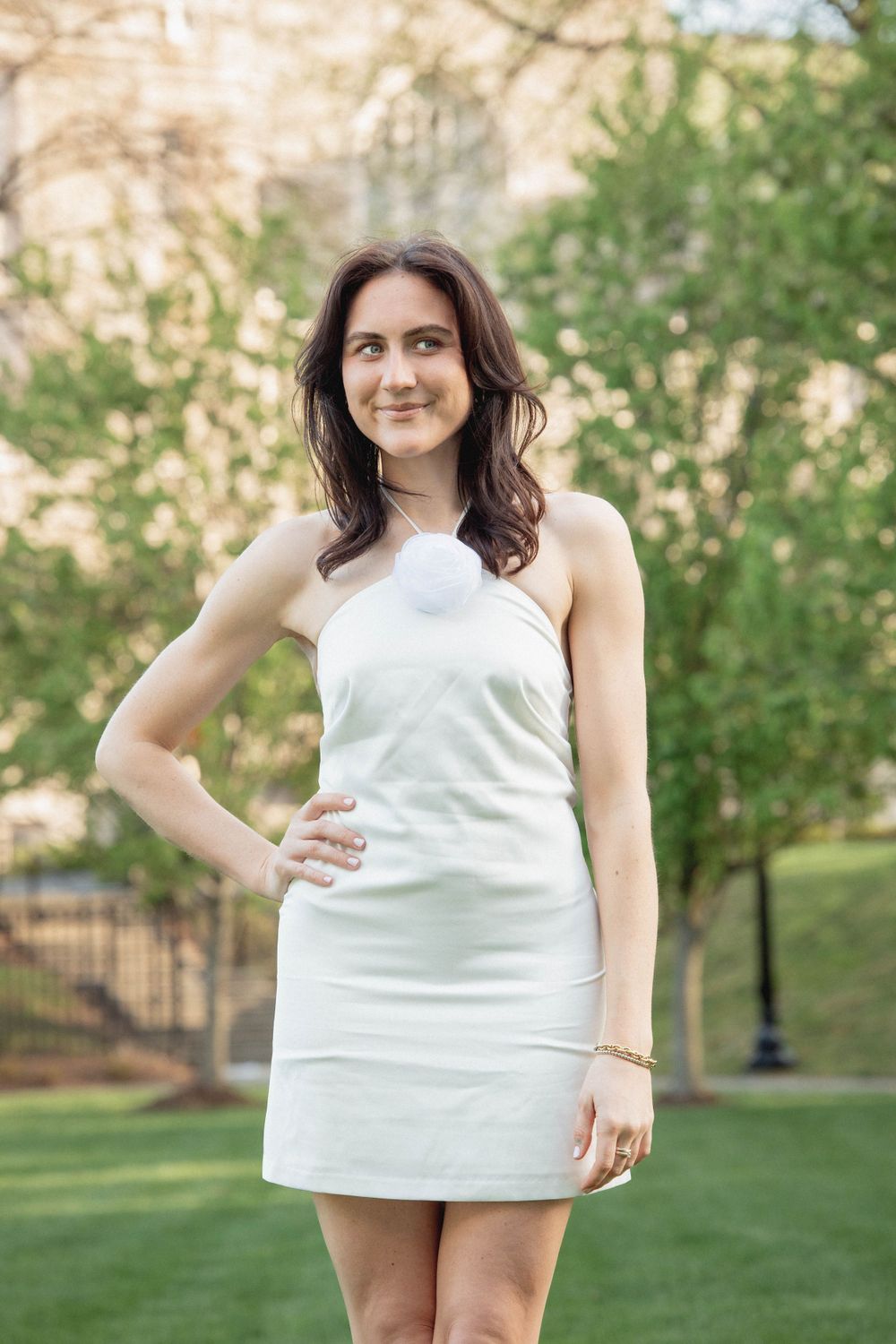 Young woman in a short white dress poses confidently on a manicured lawn.