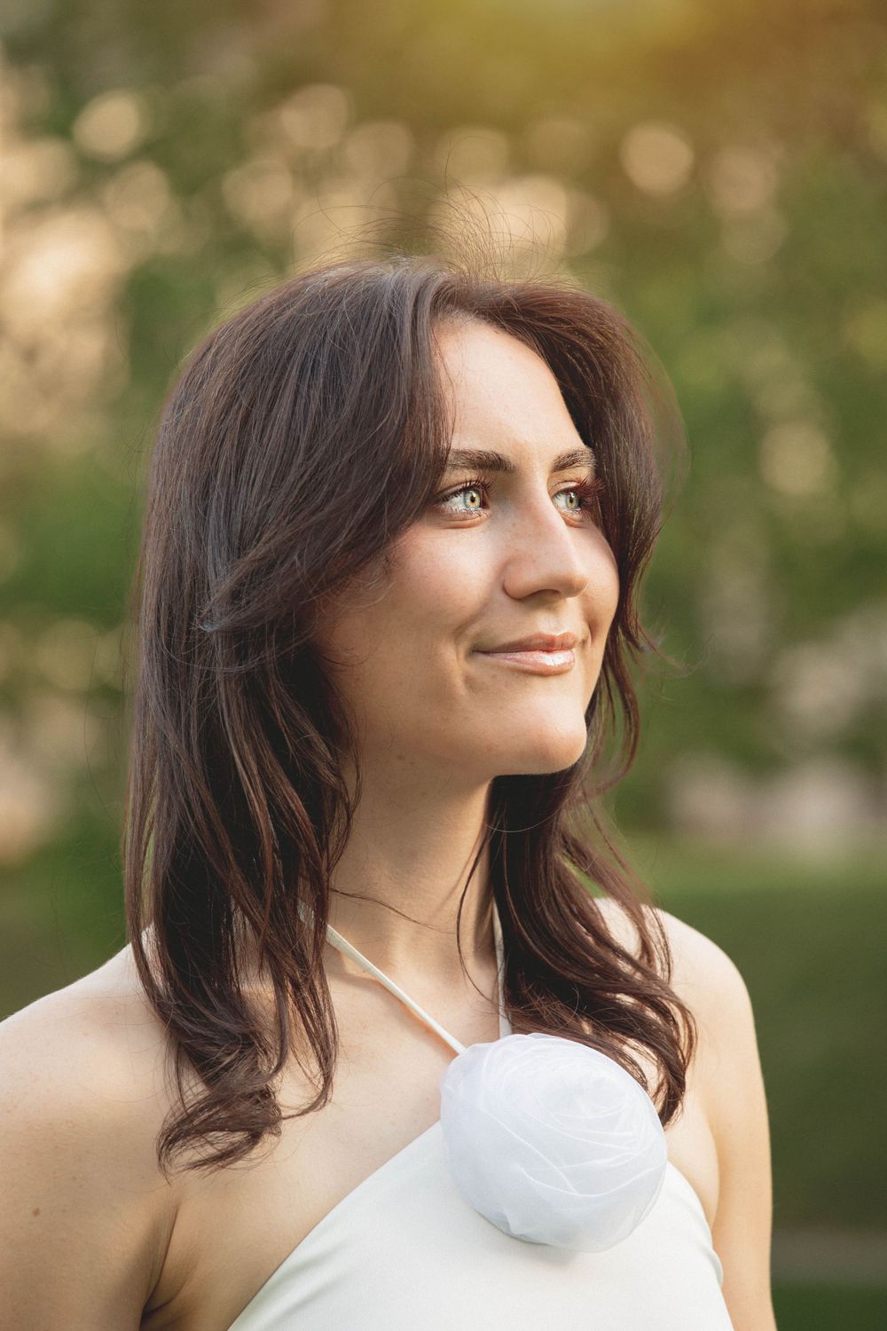 Portrait of a woman in white dress smiling elegantly against blurred outdoor background.
