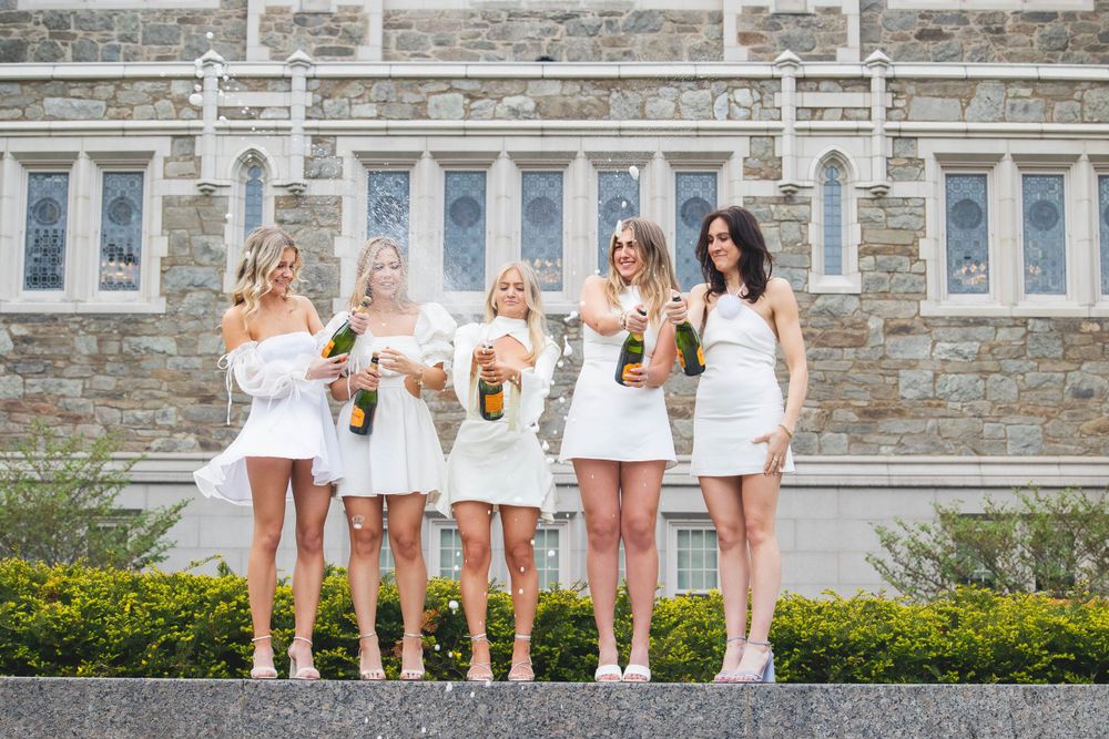 Group of friends in matching white dresses posing together on steps of stone building.