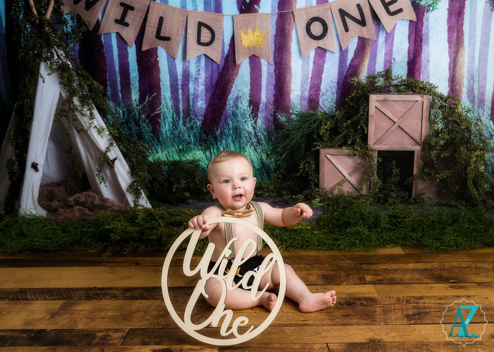 A 'Wild One' themed first birthday photoshoot setup with rustic woodland backdrop and circular prop on wooden floor.