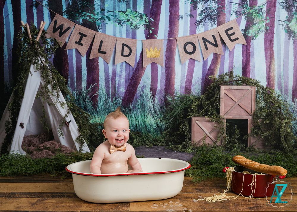 Rustic first birthday scene with vintage bathtub and 'Wild One' banner against forest backdrop.
