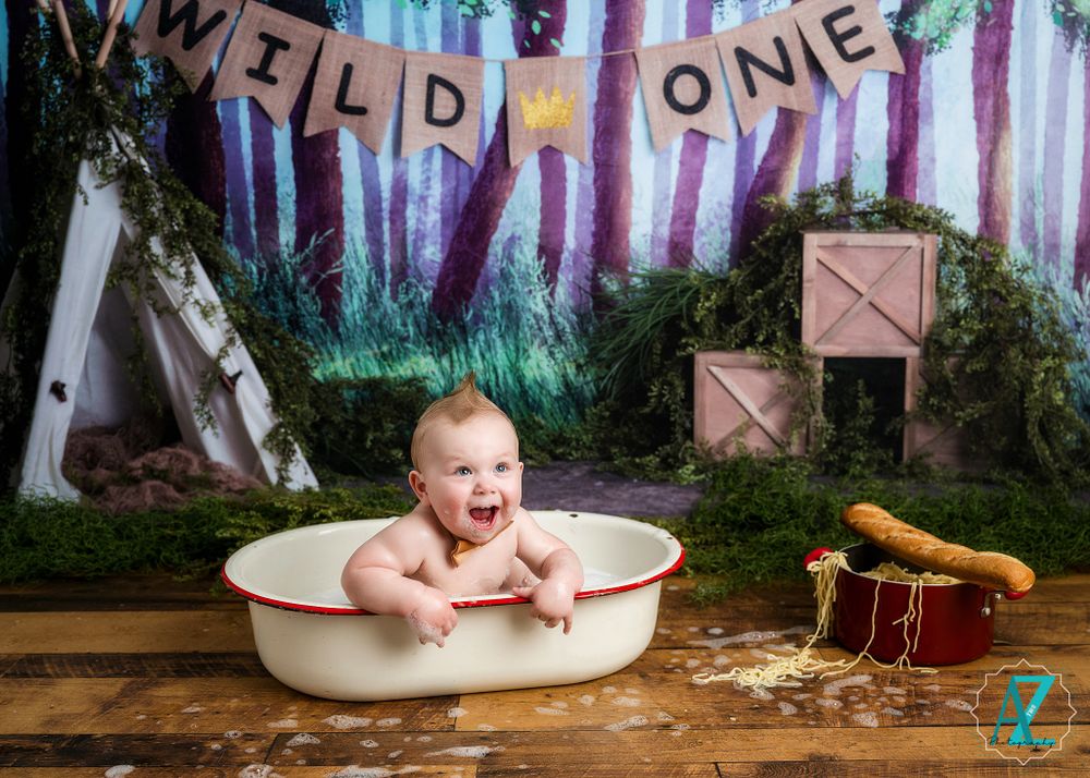 Whimsical first birthday setup with vintage bathtub against enchanted forest backdrop.