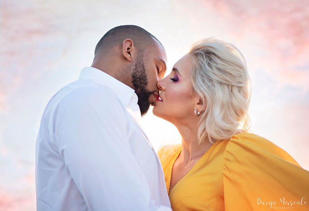 Couple sharing romantic moment against sunset sky, one wearing vibrant yellow dress.