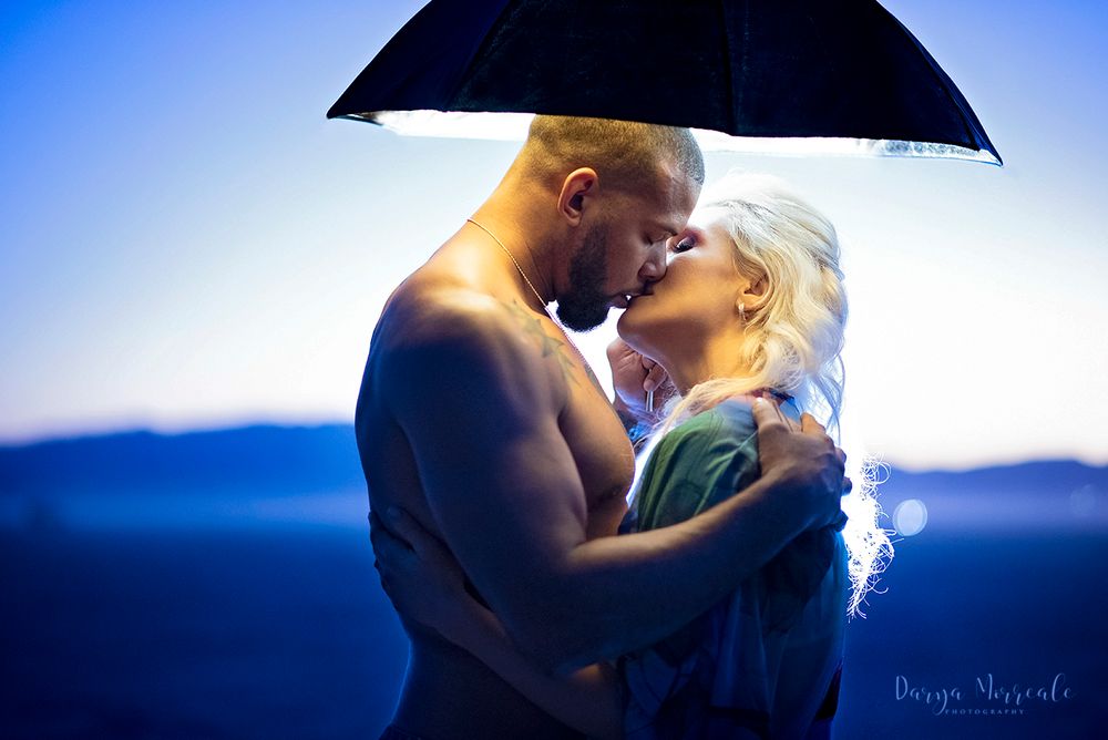 Couple embracing under black umbrella against blue twilight sky.