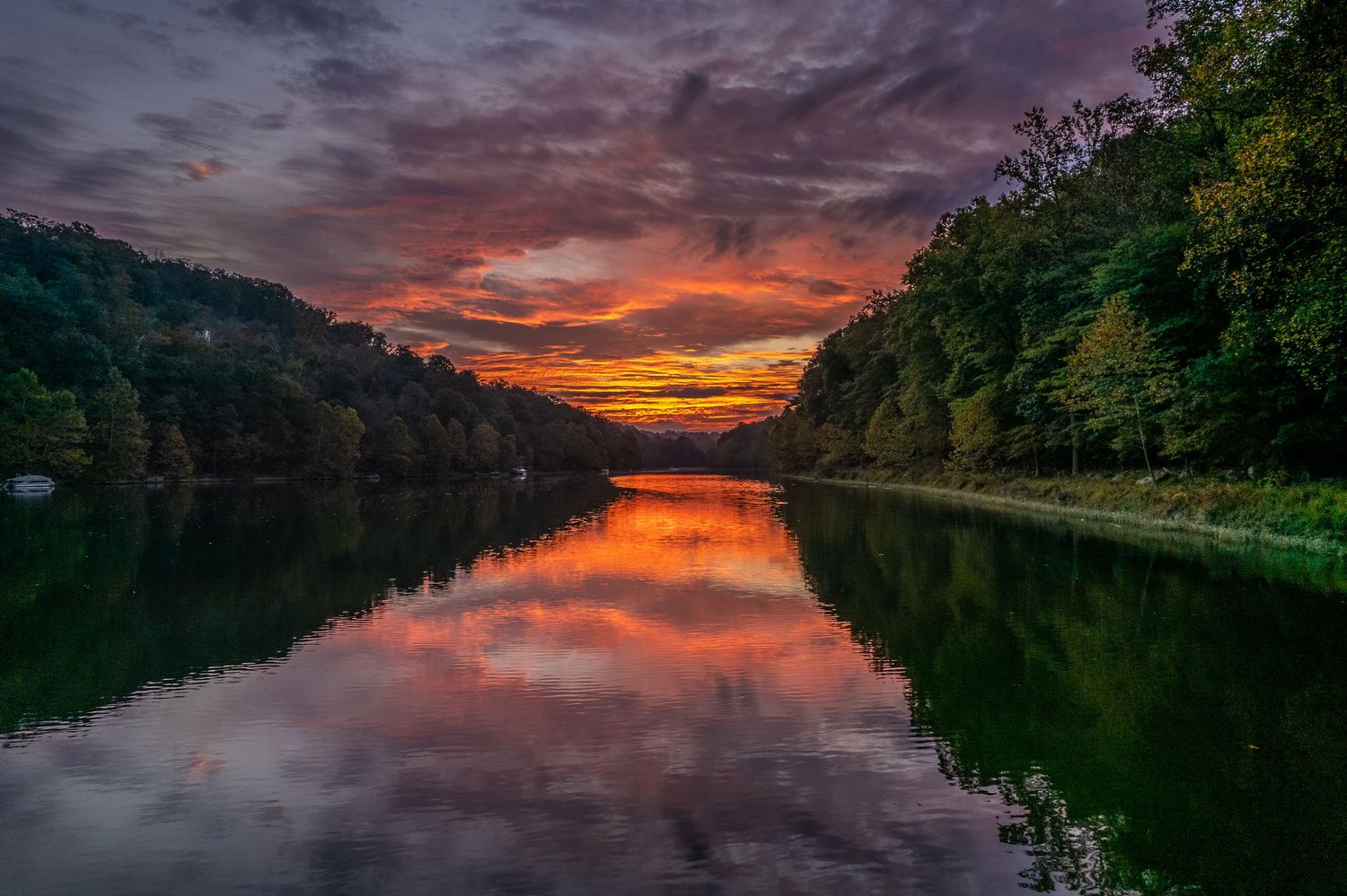 Stunning sunset reflection on a calm lake surrounded by autumn forest hills.
