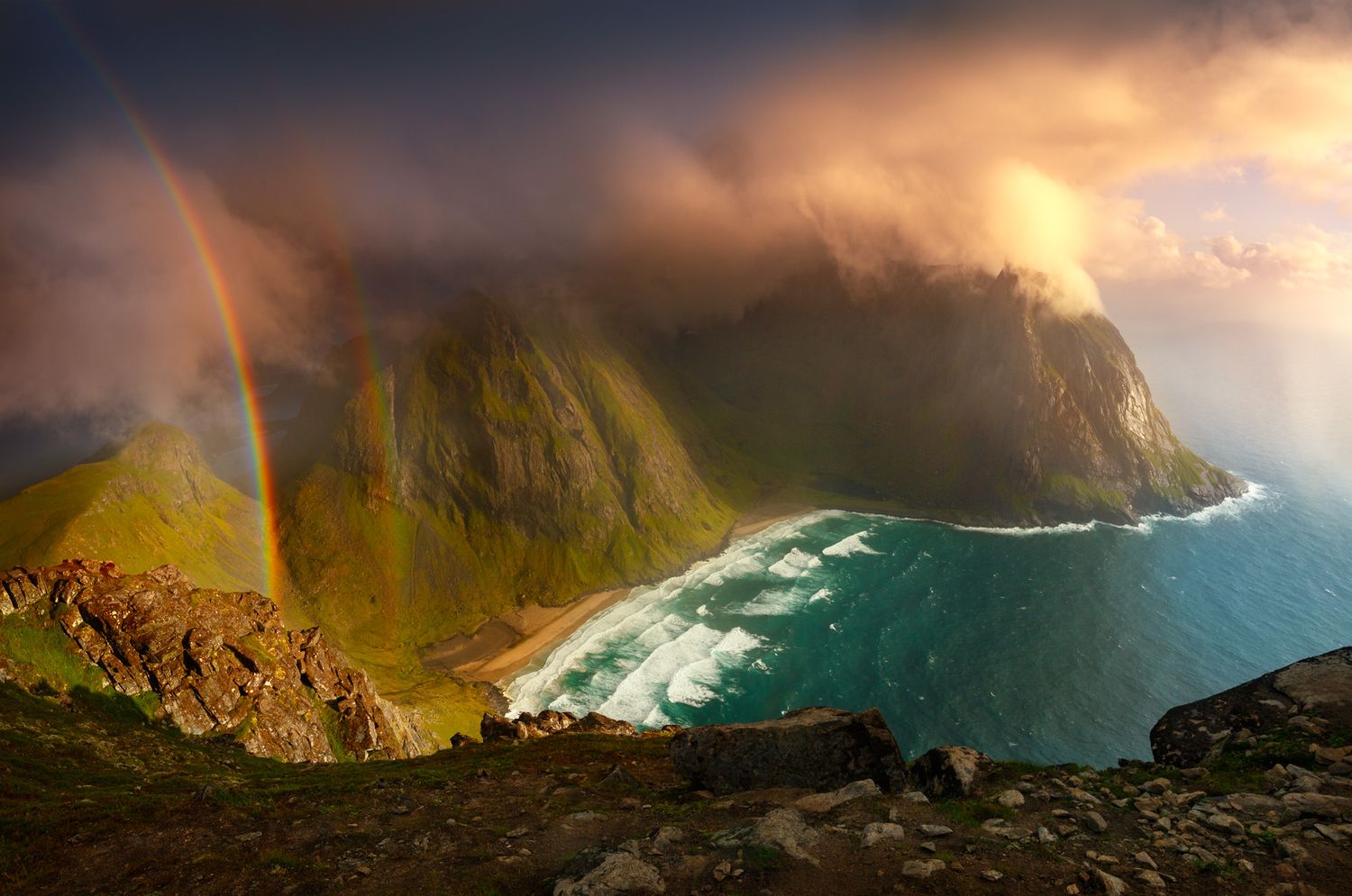 Stunning coastal landscape with double rainbow over rocky cliffs and turquoise waters at sunset.