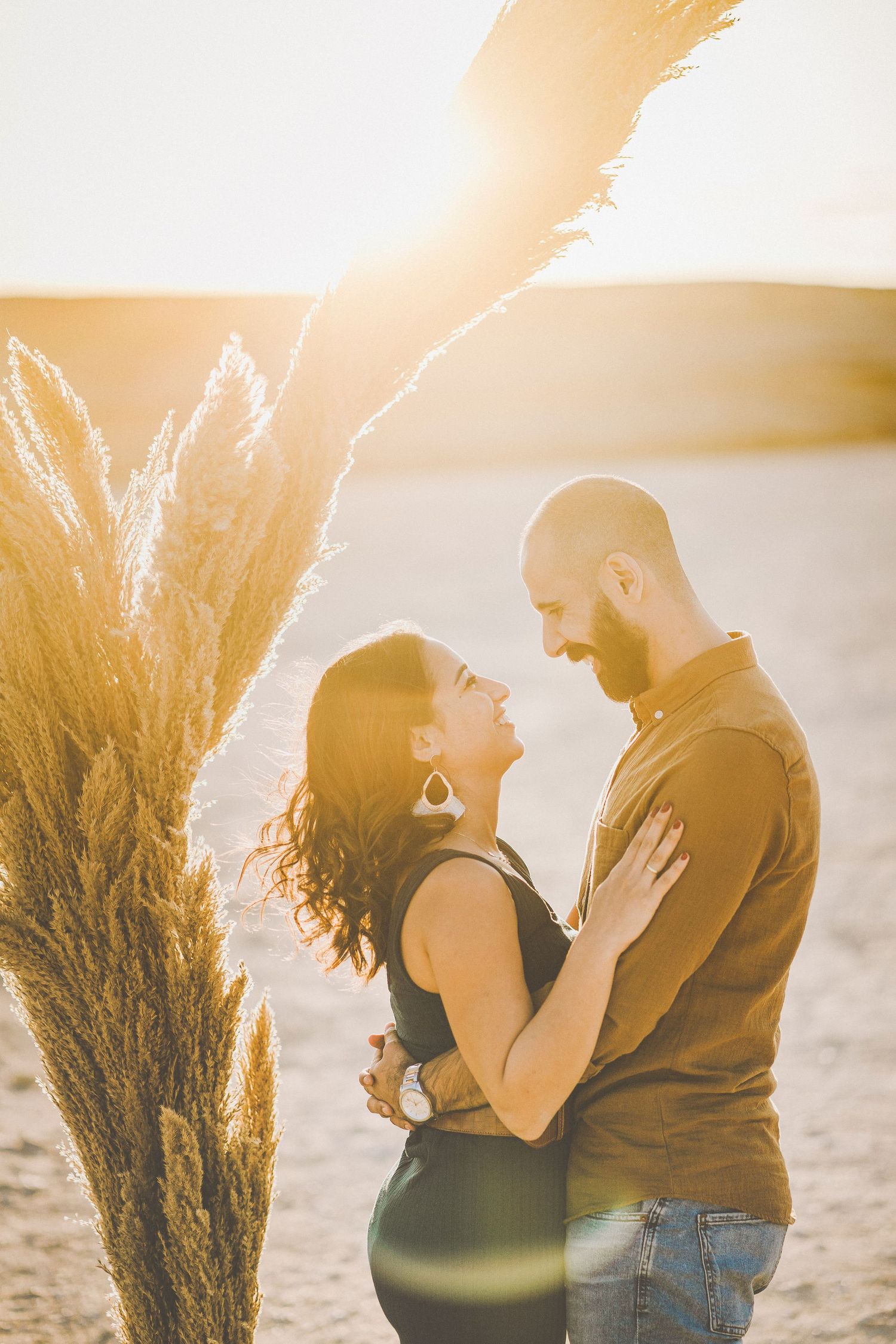 A romantic sunset engagement photo with pampas grass framing the couple.