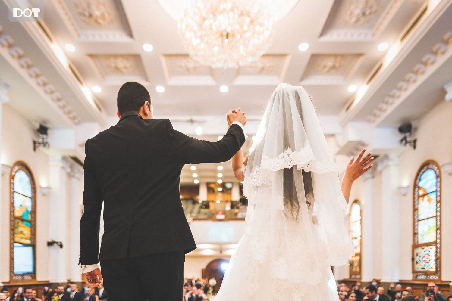A wedding ceremony moment captured in an elegant church with stained glass windows and chandeliers.