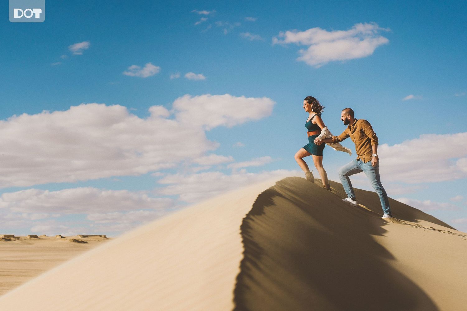 Couple playing and running together on scenic sand dunes under bright blue skies.