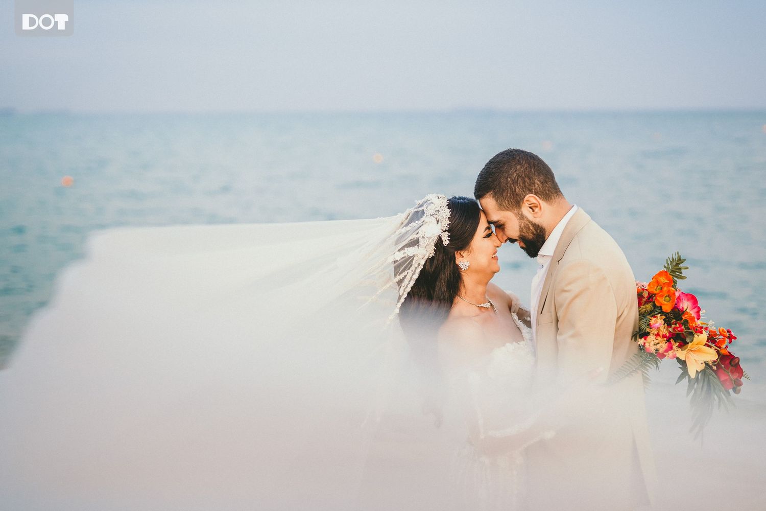A romantic wedding portrait with flowing veil and ocean backdrop.