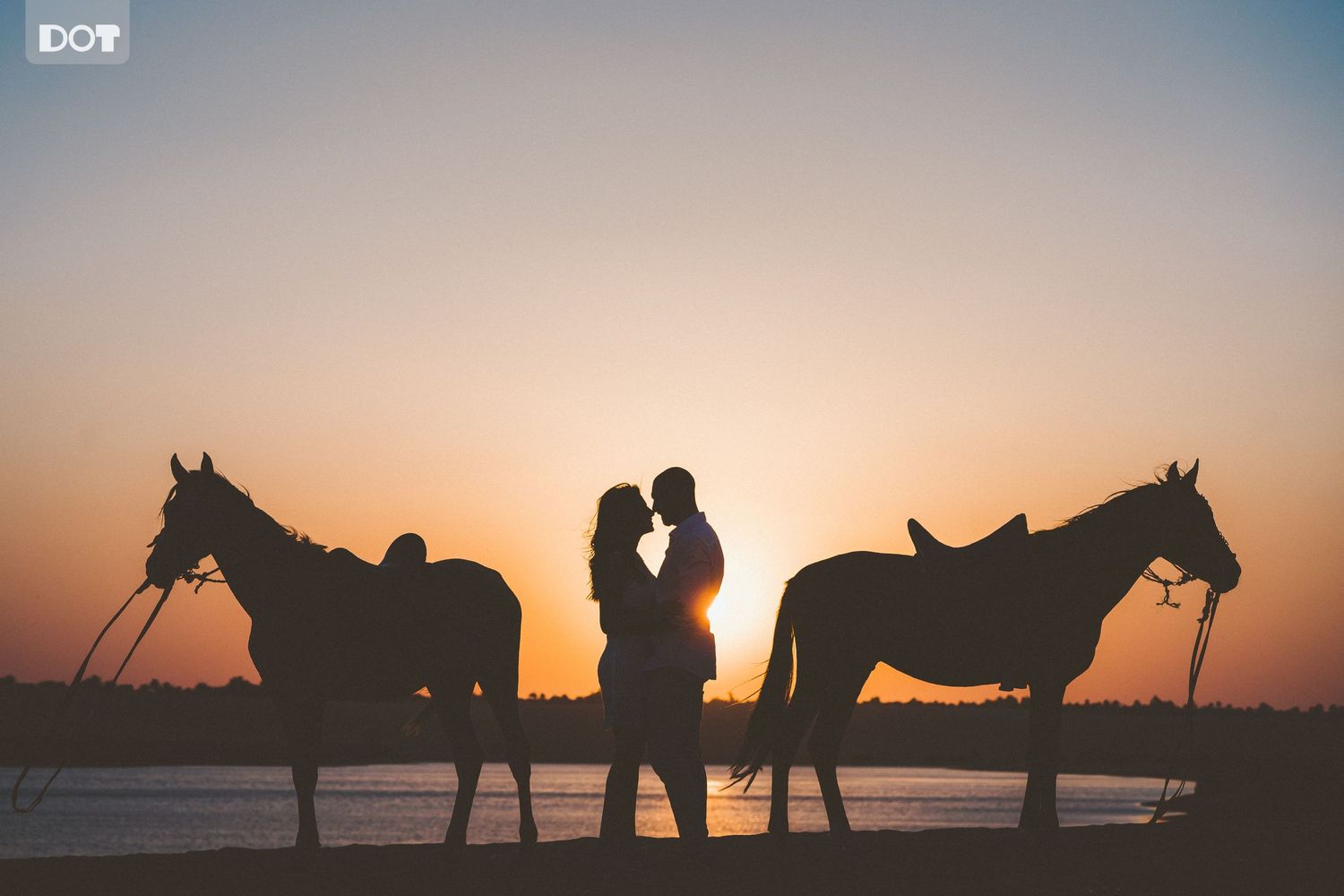 Silhouettes of horses and riders against a dramatic sunset on a beach create a romantic atmosphere.