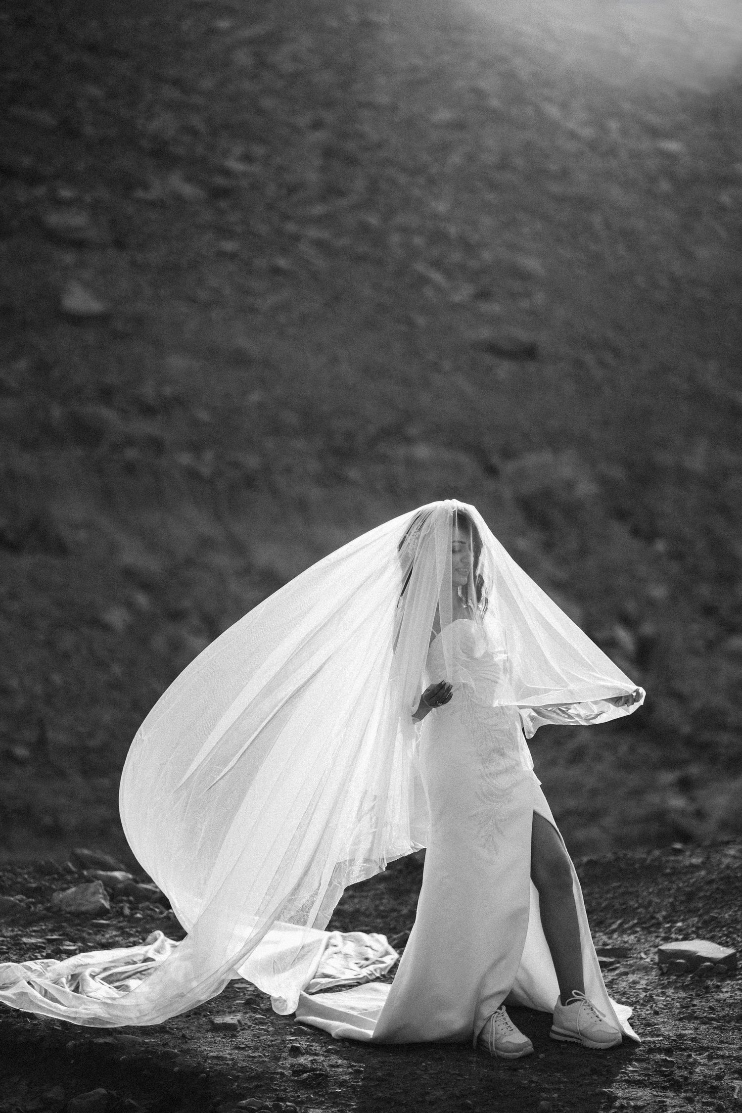 Artistic black and white photo of flowing wedding dress movement on textured ground.
