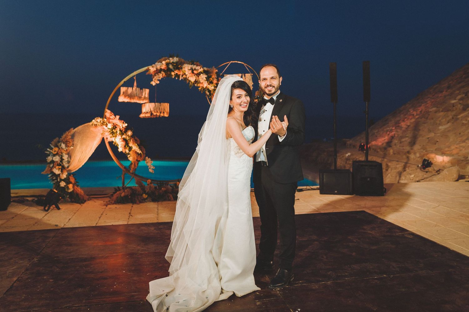 Wedding couple poses against dramatic night sky with illuminated stone backdrop.