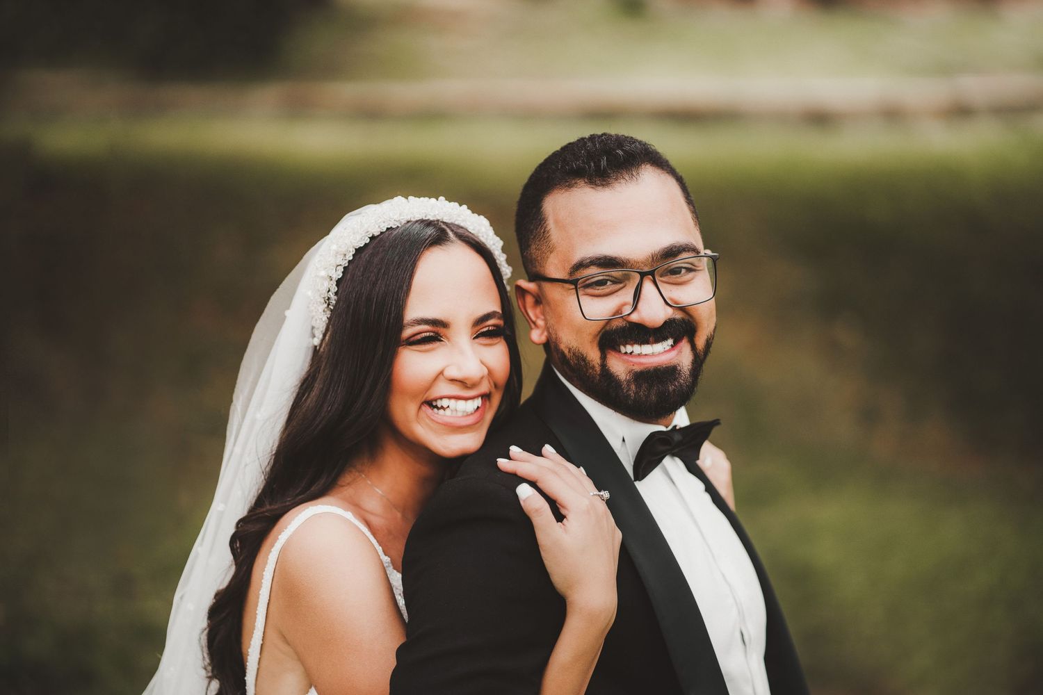Wedding couple shares joyful laughter in sunlit outdoor setting.