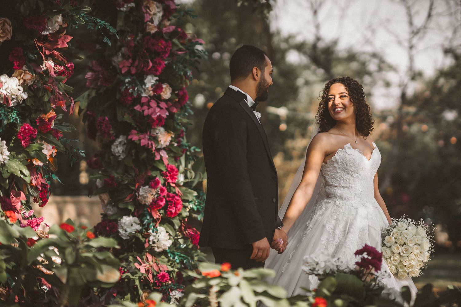 Wedding couple embraces near blooming pink bougainvillea flowers in an outdoor garden setting.