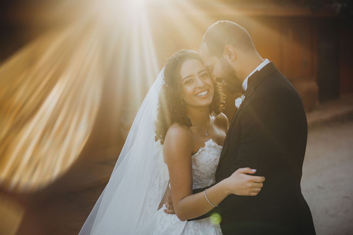 Sunbeams create dramatic lighting effect during intimate wedding moment.
