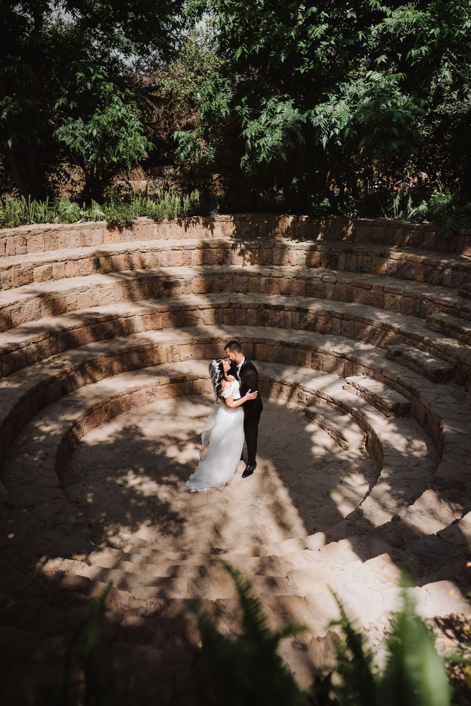 Aerial view of couple dancing in circular stone amphitheater surrounded by trees.