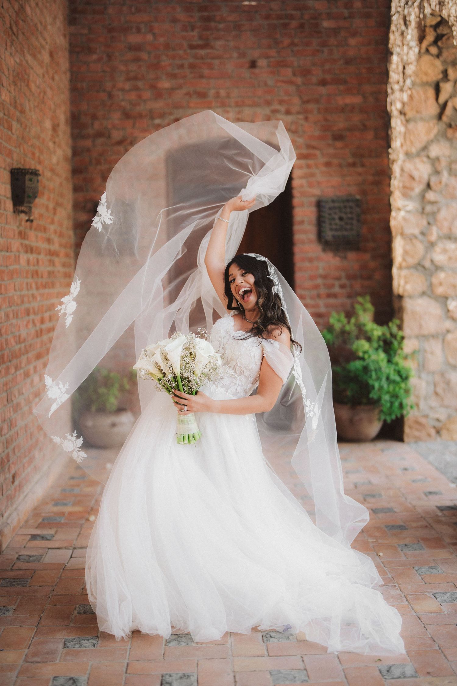 Bride in flowing white dress twirling on brick patio with floating veil.