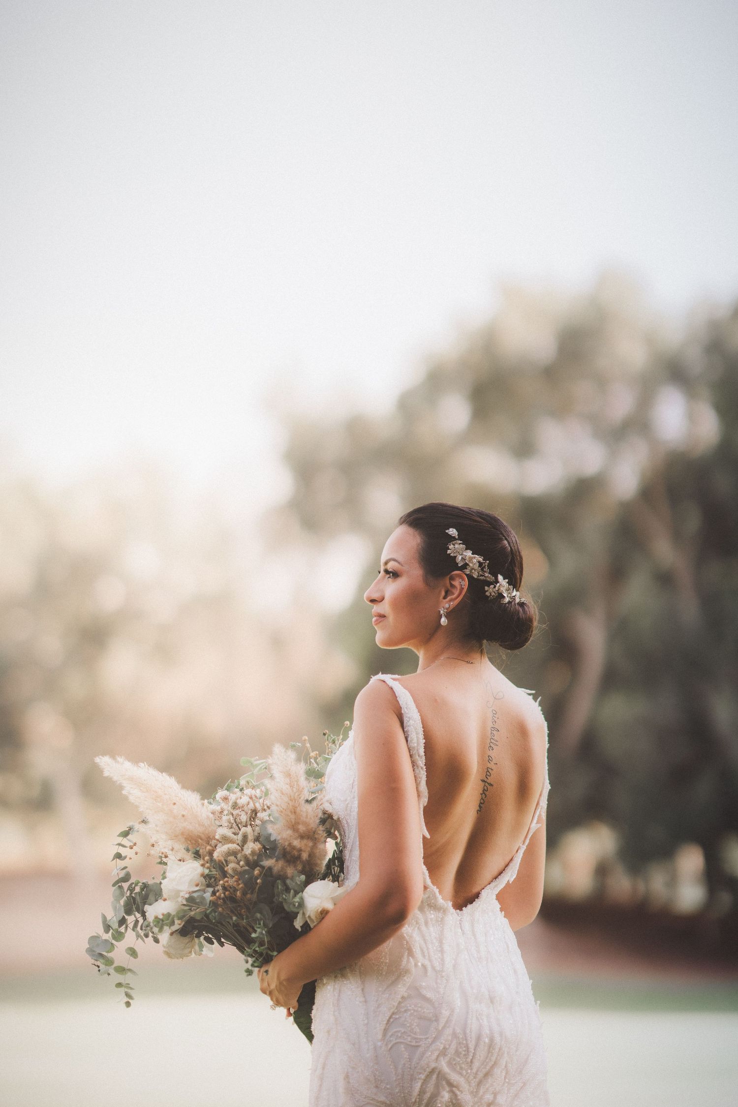 Ethereal bridal portrait in soft sunlight holding white floral bouquet.