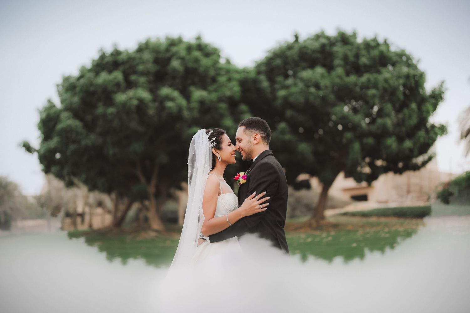 Wedding couple shares intimate moment under trees in outdoor garden setting.