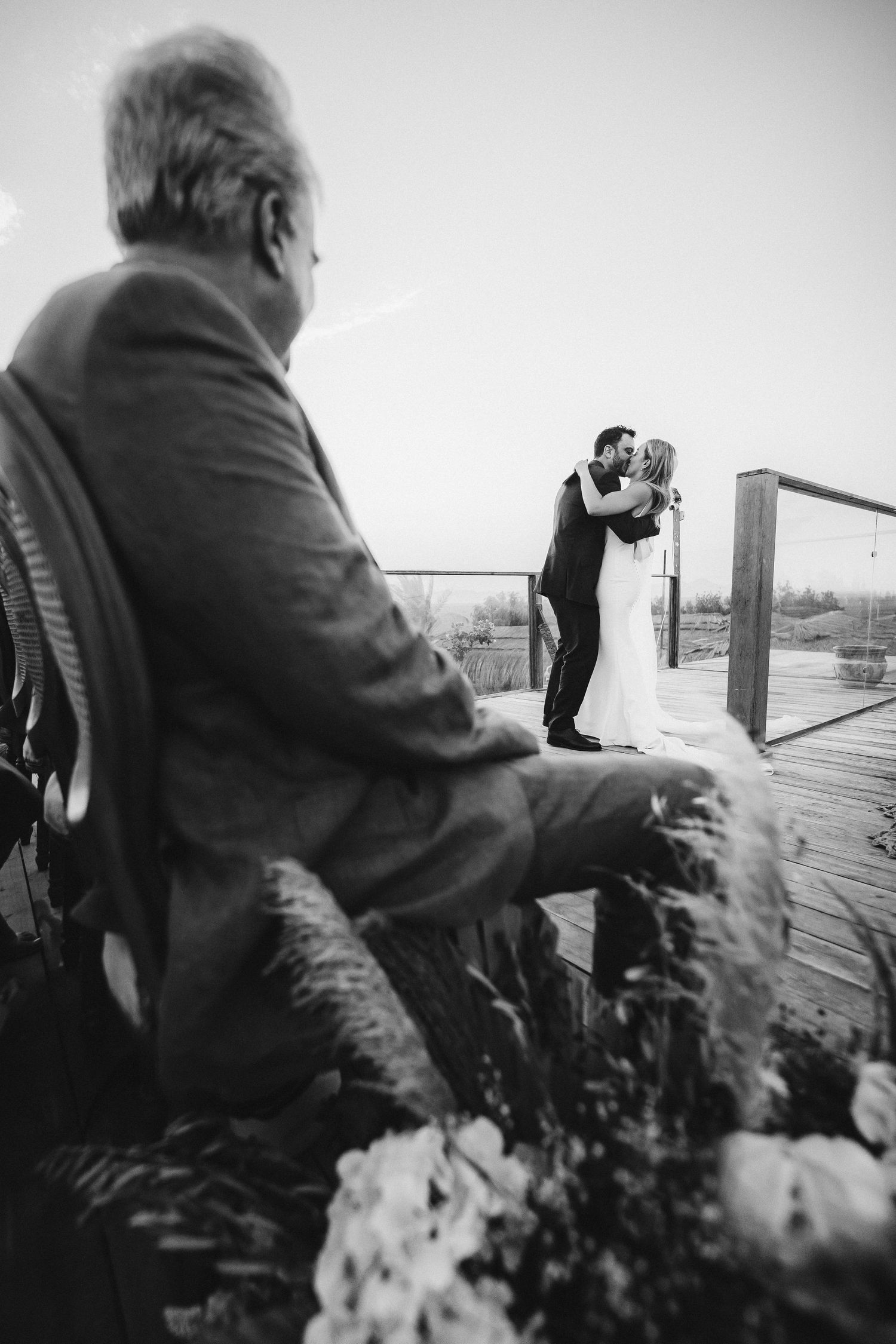 Black and white photo of wedding ceremony viewed from behind seated guest.