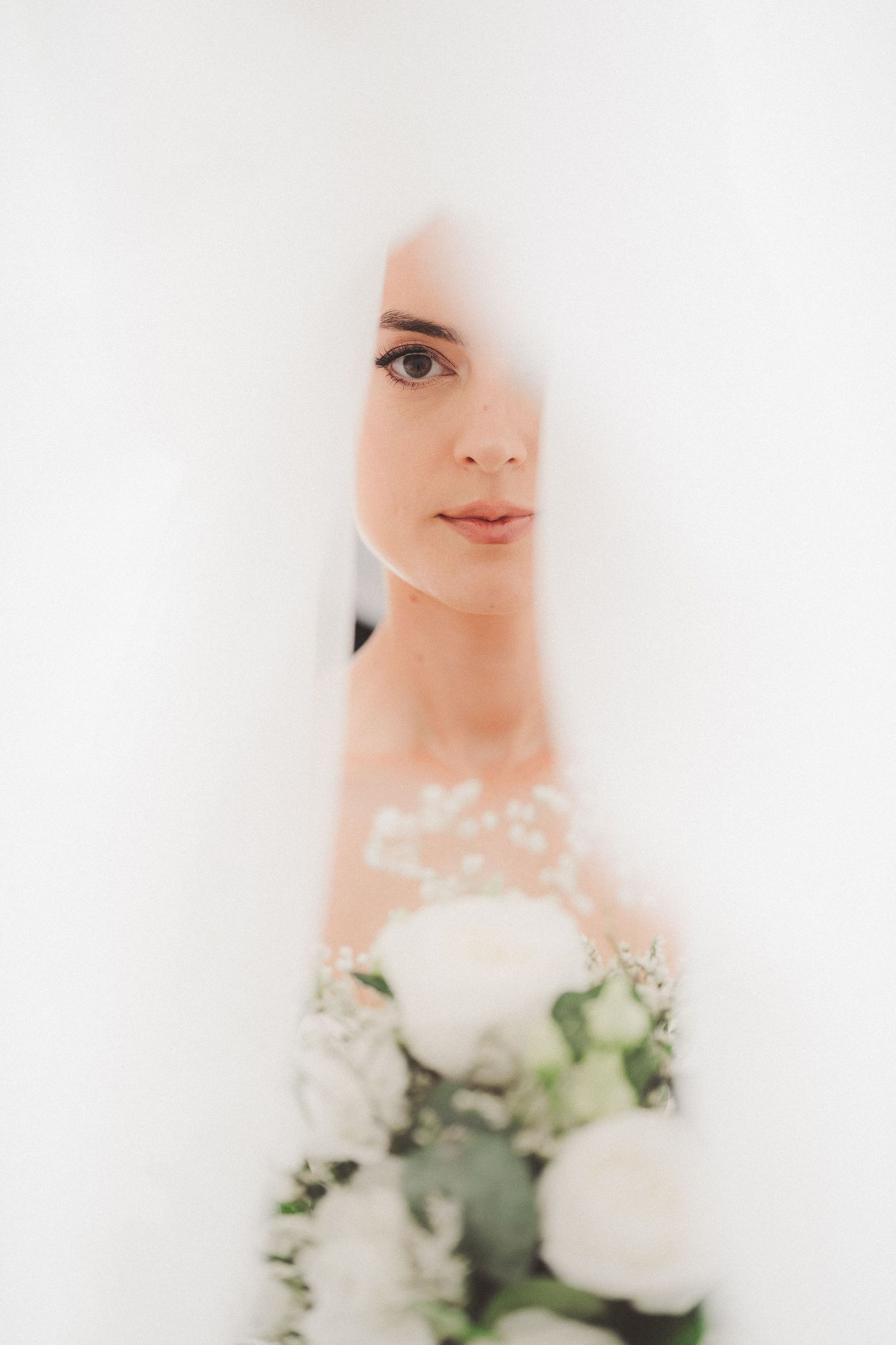 Dreamy soft focus bridal portrait with white flowers in ethereal lighting.