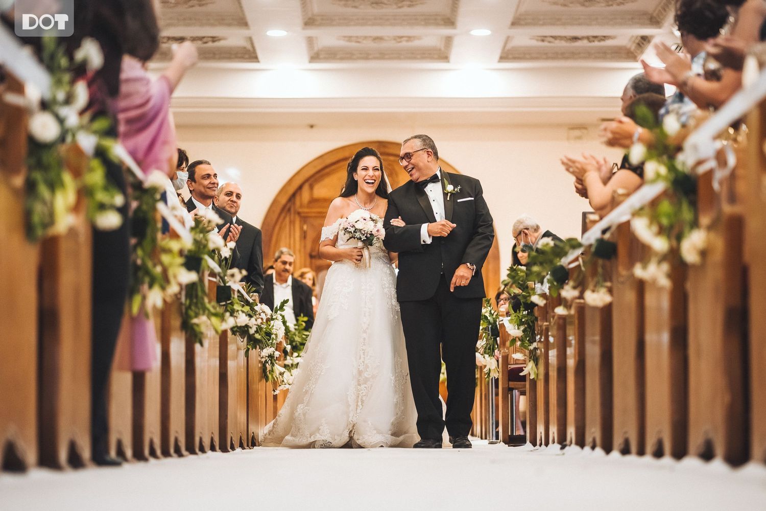 Wedding ceremony in grand church with guests seated in wooden pews along decorated aisle.