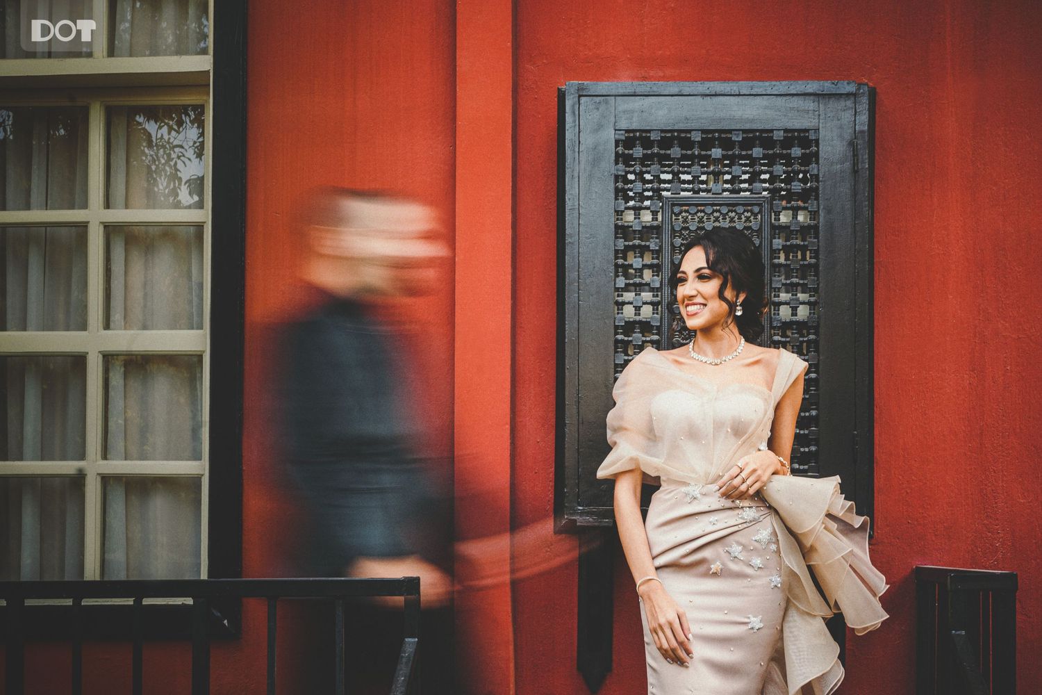 Wedding couple walking along vibrant red wall exterior of historic building.