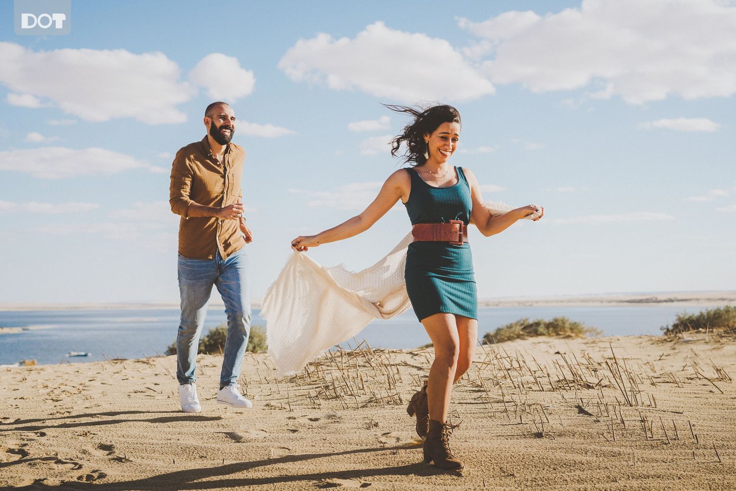 Playful couple running and dancing on sandy beach with ocean views.