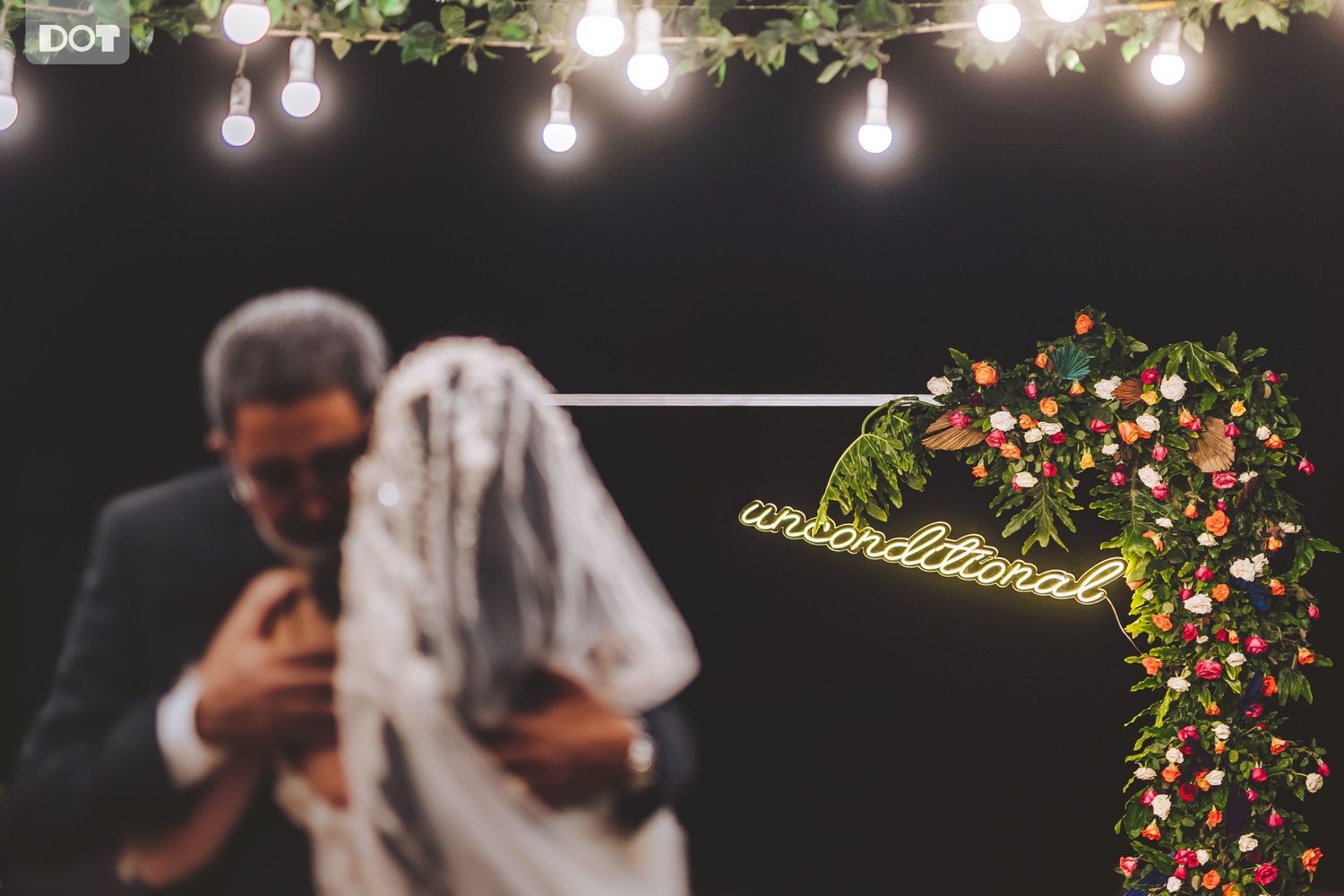 Evening outdoor wedding reception with hanging string lights and floral decorations.