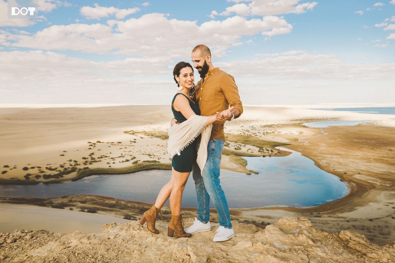 A couple embraces on a scenic cliff overlooking a winding river and desert landscape at sunset.