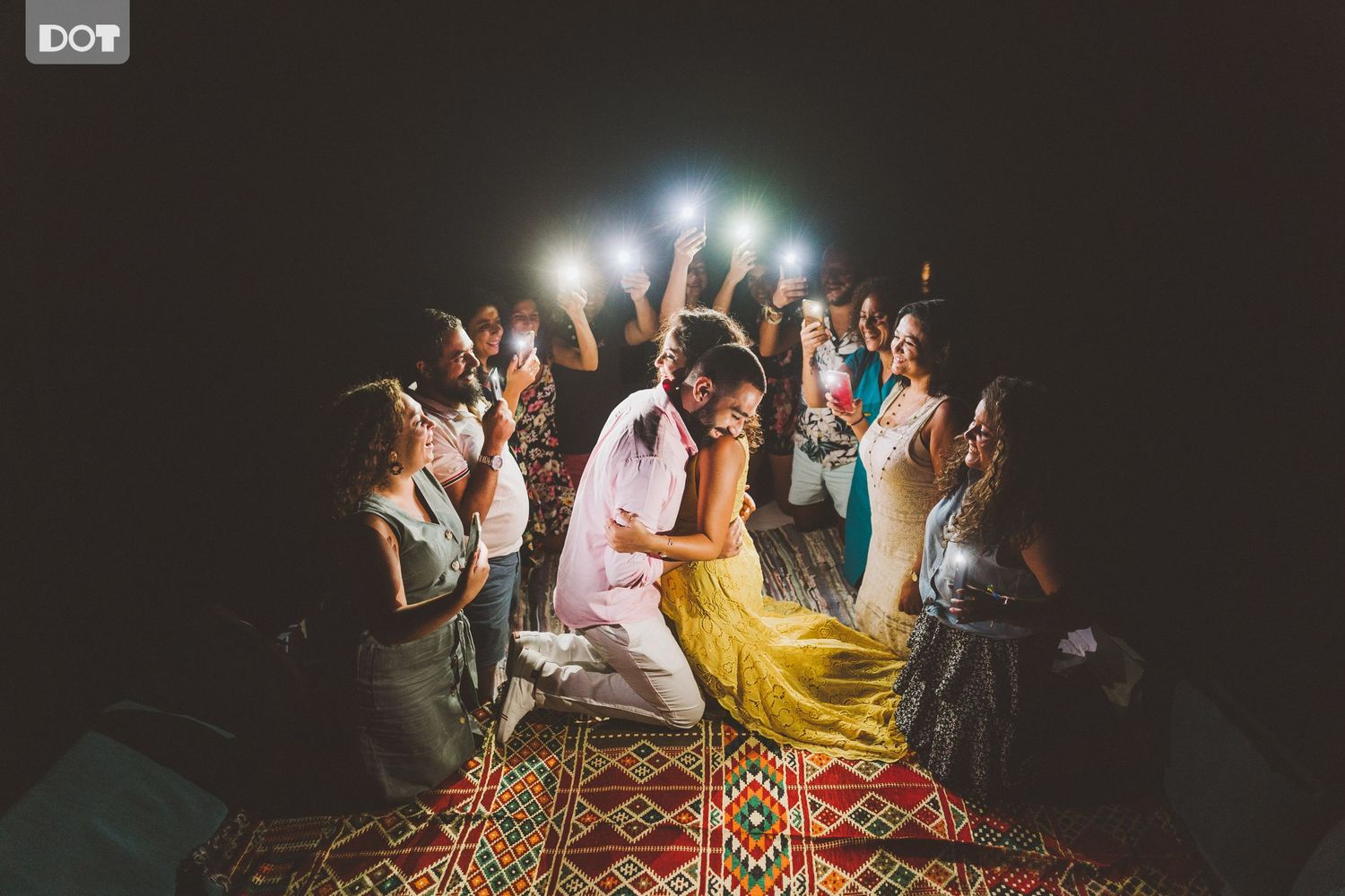 A lively wedding celebration with guests dancing and holding sparklers on a patterned rug at night.